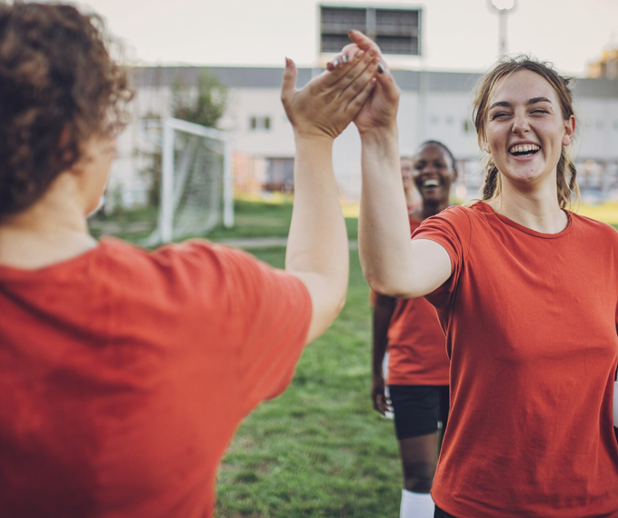 A happy girl with straight teeth, celebrating on the soccer field with her teammates, high-fiving after completing a successful braces treatment.